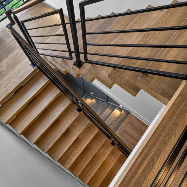 Looking down a wood stair with black metal railing and balusters toward the lower floor, with step lights set in the wall