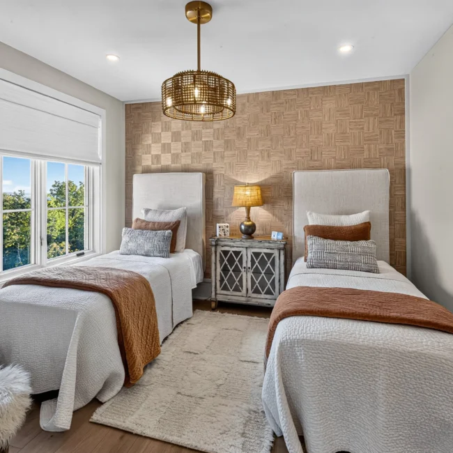 Sunset Heights bedroom with two twin beds with white upholstered headboards, rust throws, a woven checkerboard accent wall and a brass pendant