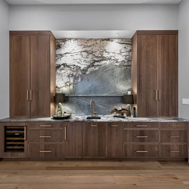 Wet bar wall with dark walnut cabinets, a marble backsplash between tall cabinets and a wine cooler under the counter