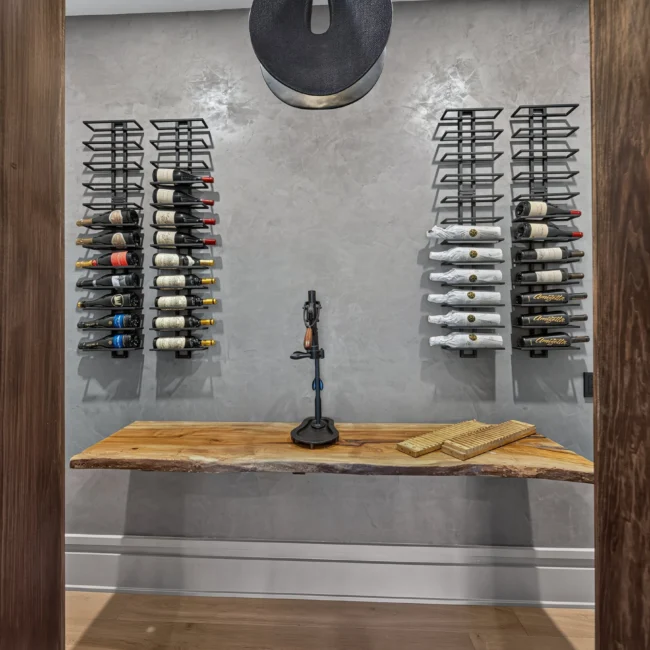Wine nook with wall-mounted bottle racks, a live-edge wood shelf and a round black pendant on a gray plaster wall
