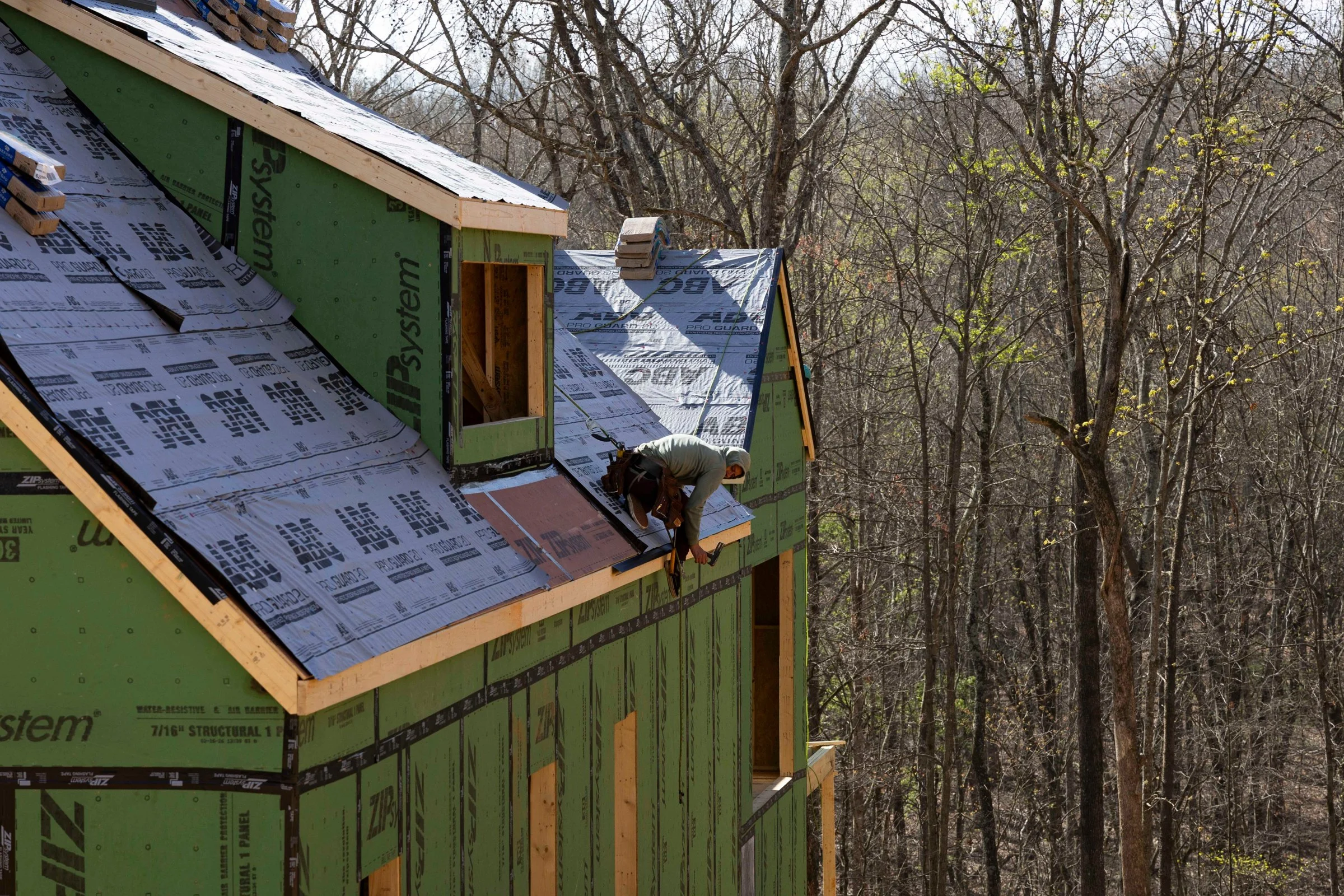 Roof sheathing and wall wrap on a home framed among bare trees, by Mike Stevens Homes